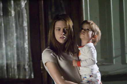Kristen Stewart holding a young boy in a dimly lit scene from the movie The Messengers, featured as an HD PC desktop wallpaper and background.