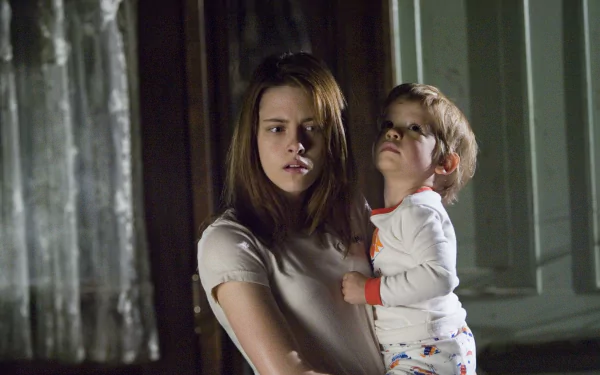 Kristen Stewart holding a young boy in a dimly lit scene from the movie The Messengers, featured as an HD PC desktop wallpaper and background.
