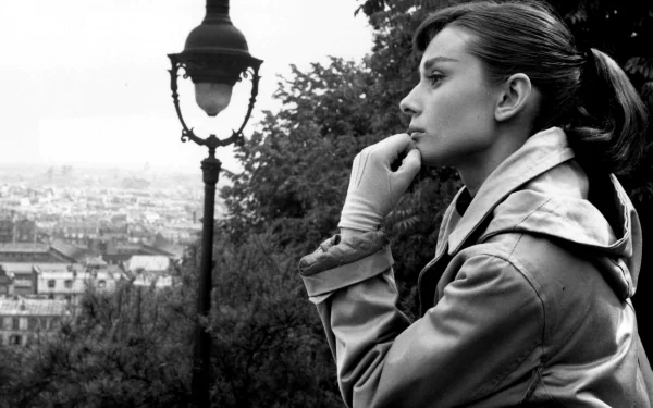 Black and white HD desktop wallpaper featuring a thoughtful Audrey Hepburn in profile, set against a cityscape with a vintage streetlamp in the background.