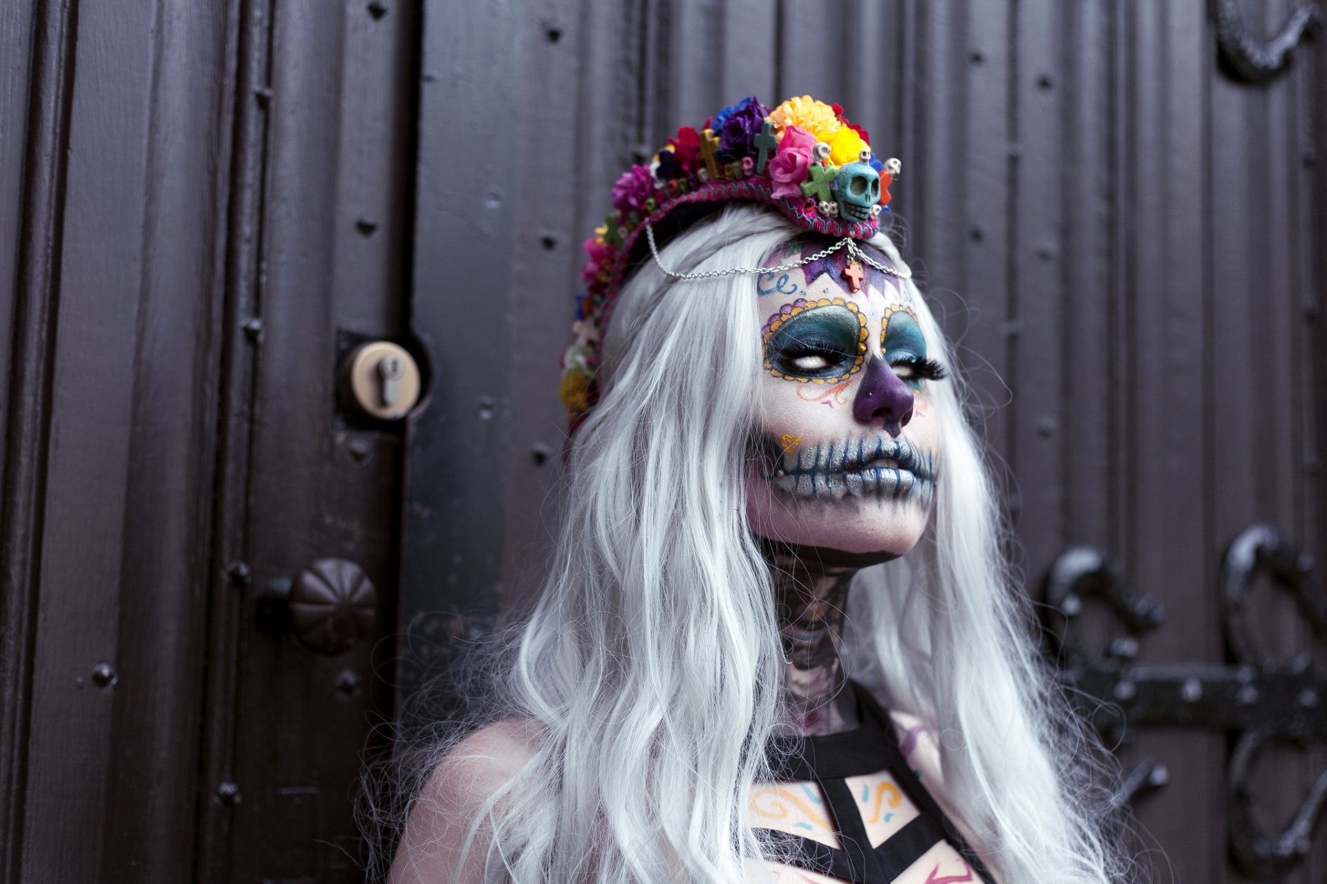 HD PC desktop wallpaper: artistic sugar skull makeup on a figure with long white hair and a floral crown, skeletal face paint and vivid colors against a dark metal background.