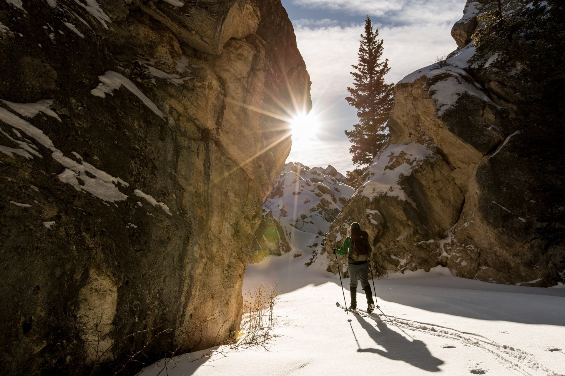 A skier traverses snowy terrain in Yellowstone wilderness, framed by rugged mountains and sunbeams, capturing the serene beauty of winter sports in a high-definition desktop wallpaper.