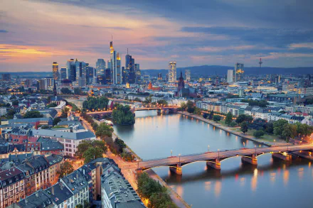 A vibrant cityscape of Frankfurt, Germany, featuring skyscrapers, bridges over the river, and urban buildings under a colorful evening sky.