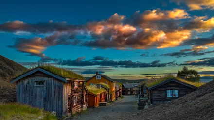 A scenic view of charming wooden houses with grass roofs in Norway, set against a vibrant sunset sky, creating a stunning desktop wallpaper and background.