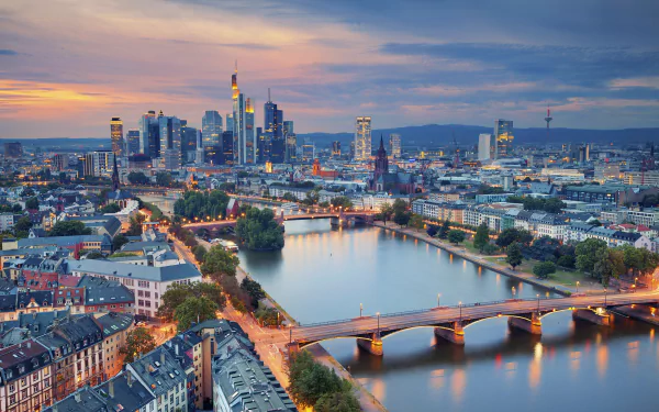 A vibrant cityscape of Frankfurt, Germany, featuring skyscrapers, bridges over the river, and urban buildings under a colorful evening sky.