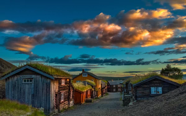 A scenic view of charming wooden houses with grass roofs in Norway, set against a vibrant sunset sky, creating a stunning desktop wallpaper and background.