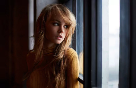 A stunning HD desktop wallpaper features Russian model Anastasiya Scheglova, a blonde woman in a mustard sweater, gazing thoughtfully out of a window.