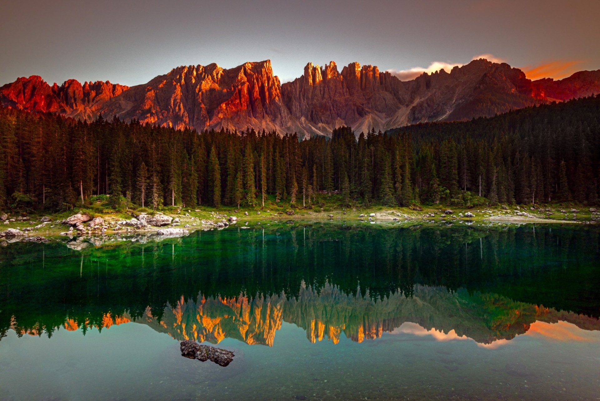 A stunning sunset over mountains reflects in a serene lake, surrounded by a lush forest, capturing the beauty of nature in this HD desktop wallpaper.