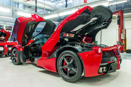 Red Ferrari LaFerrari showcased in a garage with its doors lifted, displaying its sleek design and engineering details. High-definition wallpaper for car enthusiasts.