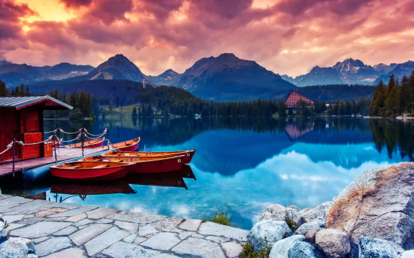 2K Quad HD PC wallpaper: sunset over a Slovak mountain lake, canoes and a boat tied to a wooden dock, mirrored peaks and a small lakeside vehicle near a chalet.