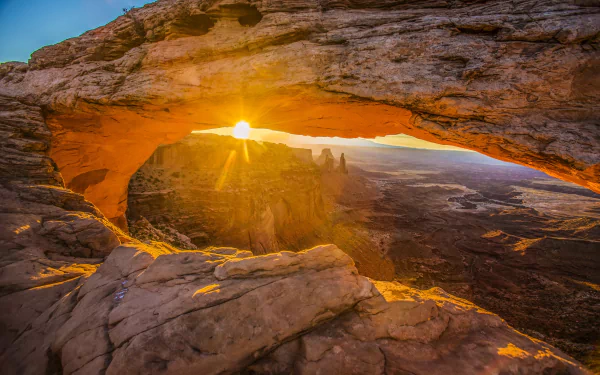 Sunbeam through Mesa Arch in a USA national park, illuminating canyon and distant mountain spires — 4K Ultra HD PC desktop wallpaper and background of dramatic nature.