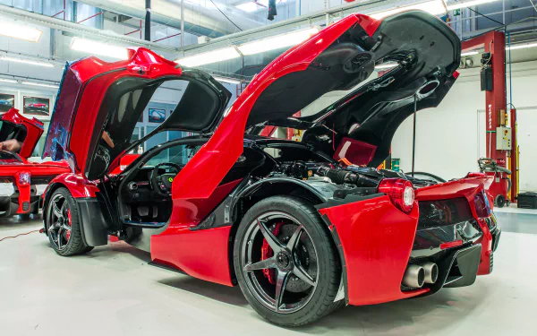 Red Ferrari LaFerrari showcased in a garage with its doors lifted, displaying its sleek design and engineering details. High-definition wallpaper for car enthusiasts.