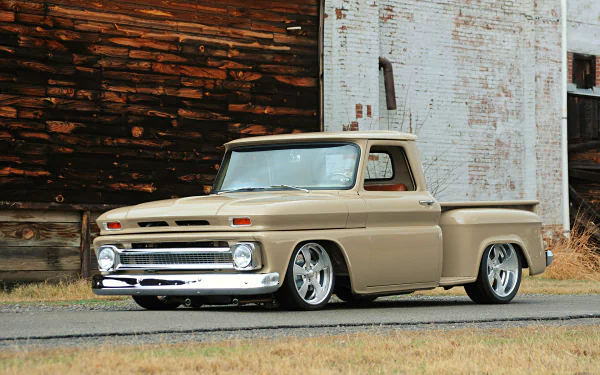 A beige 1965 Chevrolet C10 hot rod truck with lowered suspension parked in front of weathered wooden and brick walls, showcased as an HD PC desktop wallpaper.