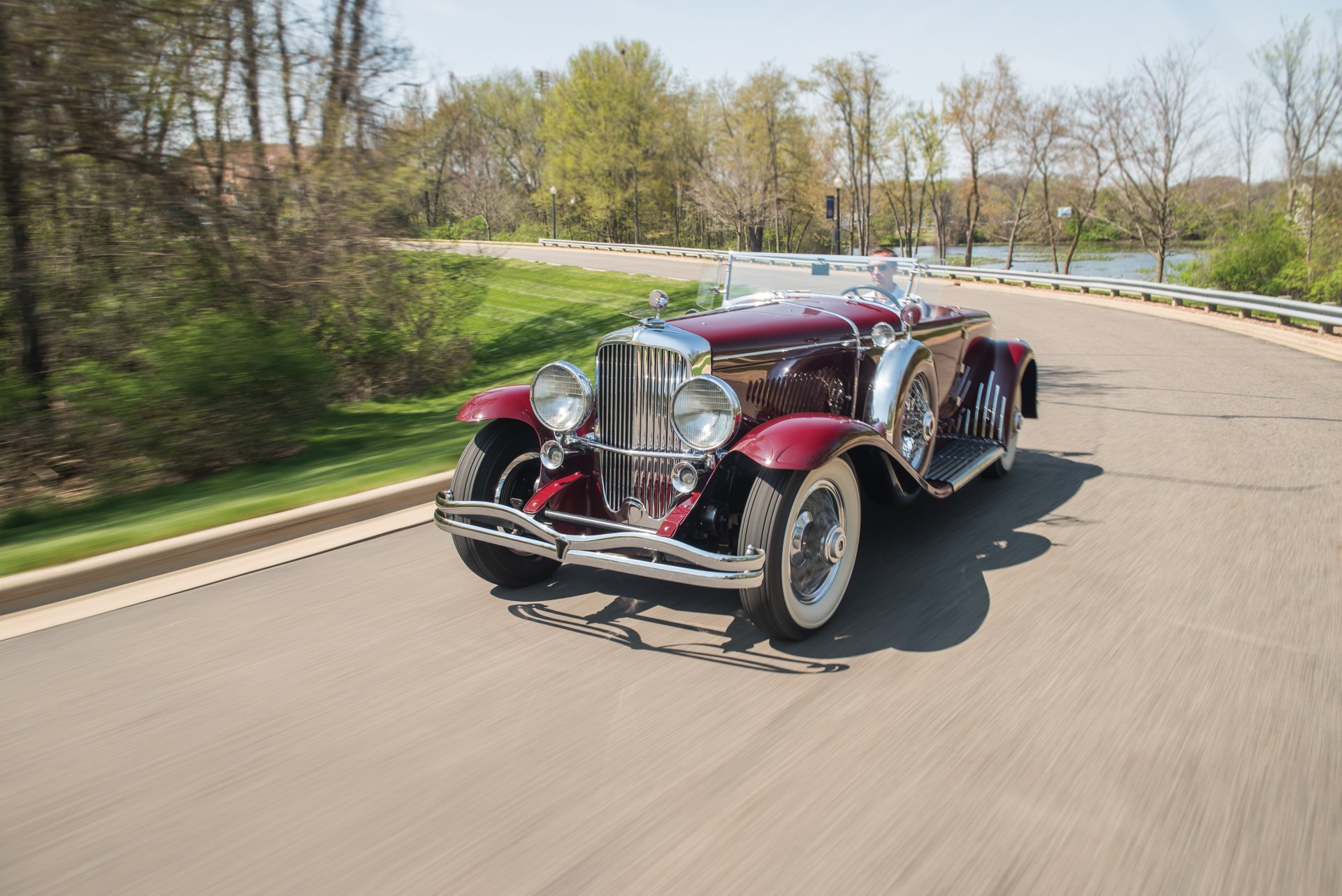 A vintage 1929 Duesenberg Model J Disappearing Top Convertible Coupe cruising on a scenic road, captured in this HD PC desktop wallpaper and background.