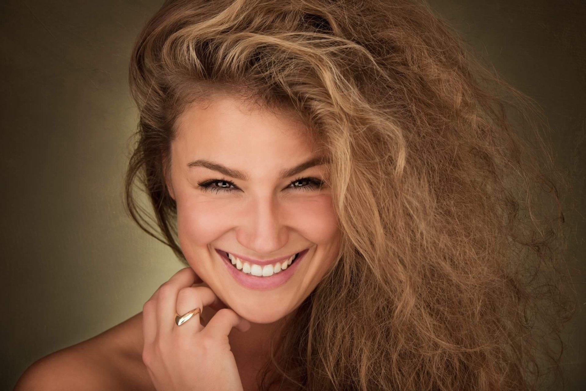 HD desktop wallpaper featuring a smiling woman model with voluminous curly hair and a radiant expression, emphasizing natural beauty and warmth.