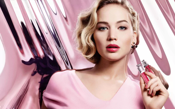 Close-up of American actress Jennifer Lawrence with blonde hair, blue eyes, and pink lipstick, set against a pink and metallic abstract background in 8K Ultra HD quality.