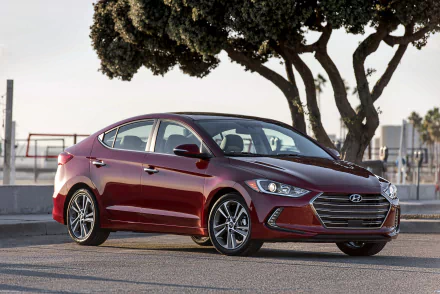 HD desktop wallpaper of a red Hyundai Elantra compact car parked outdoors near trees, showcasing the vehicle’s sleek design and modern features.
