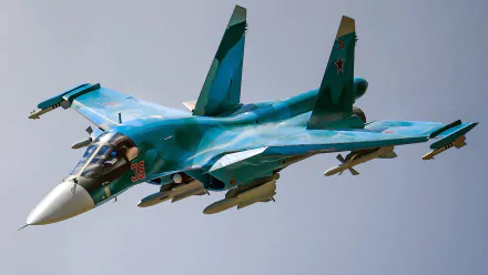 HD PC desktop wallpaper of a Sukhoi Su-34 military warplane aircraft: twin-seat jet fighter in blue camouflage banking with missile-laden wings against a clear sky.