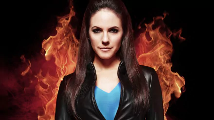 HD PC desktop wallpaper and background of a female character from the TV show Lost Girl against roaring flames, wearing a black jacket and blue top, staring confidently.