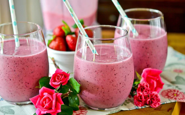HD desktop wallpaper featuring three glasses of pink berry smoothie with milk and straws, surrounded by fresh strawberries and vibrant pink roses in a still life arrangement.