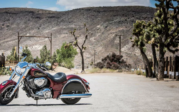 HD PC desktop wallpaper of an Indian Chief Classic motorcycle parked on a sunlit desert road with Joshua trees and rocky hills in the background.