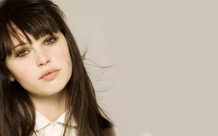 A close-up of British actress Felicity Jones, featuring her striking green eyes and soft expression, set against a muted background. Suitable as an HD desktop wallpaper.