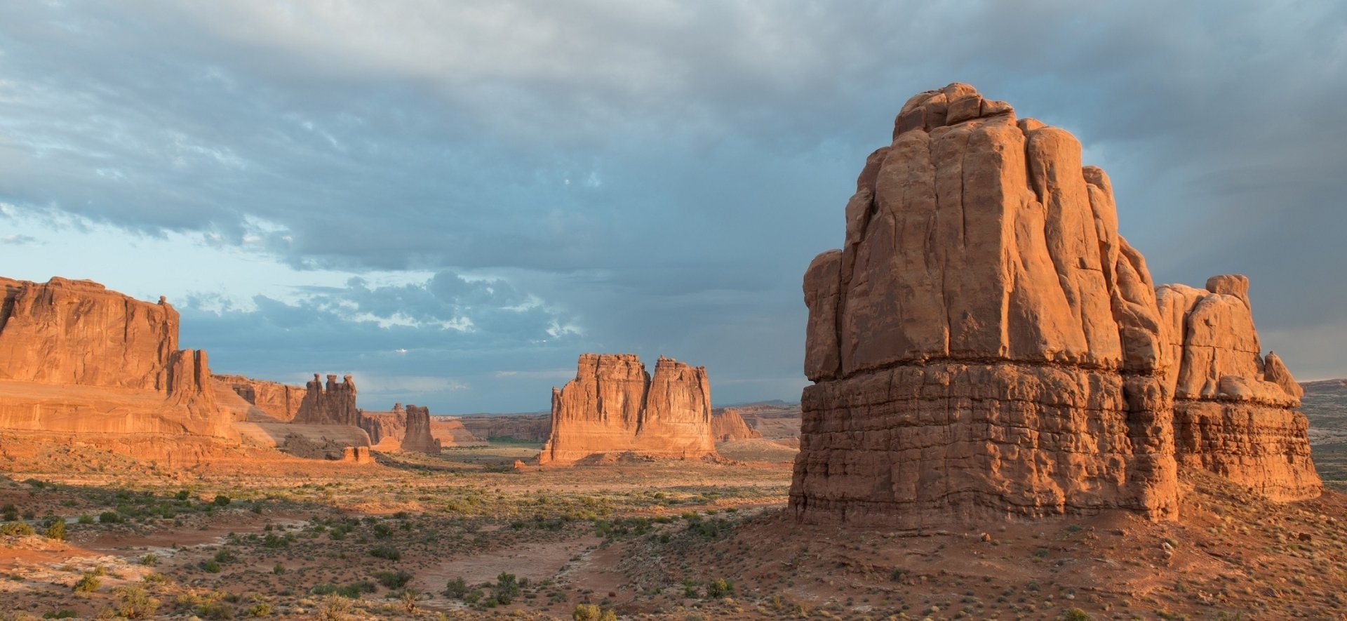 Panoramic view of Utah’s Arches National Park desert landscape, showcasing rugged red rock formations under a partly cloudy sky in vibrant HD detail.