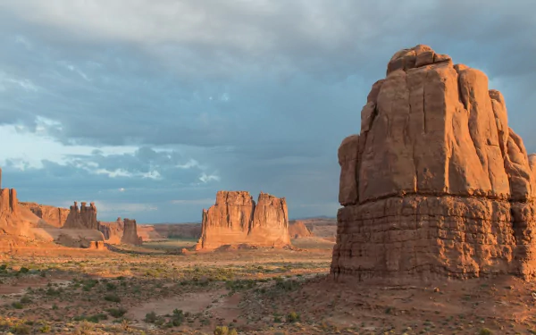 Panoramic view of Utah’s Arches National Park desert landscape, showcasing rugged red rock formations under a partly cloudy sky in vibrant HD detail.