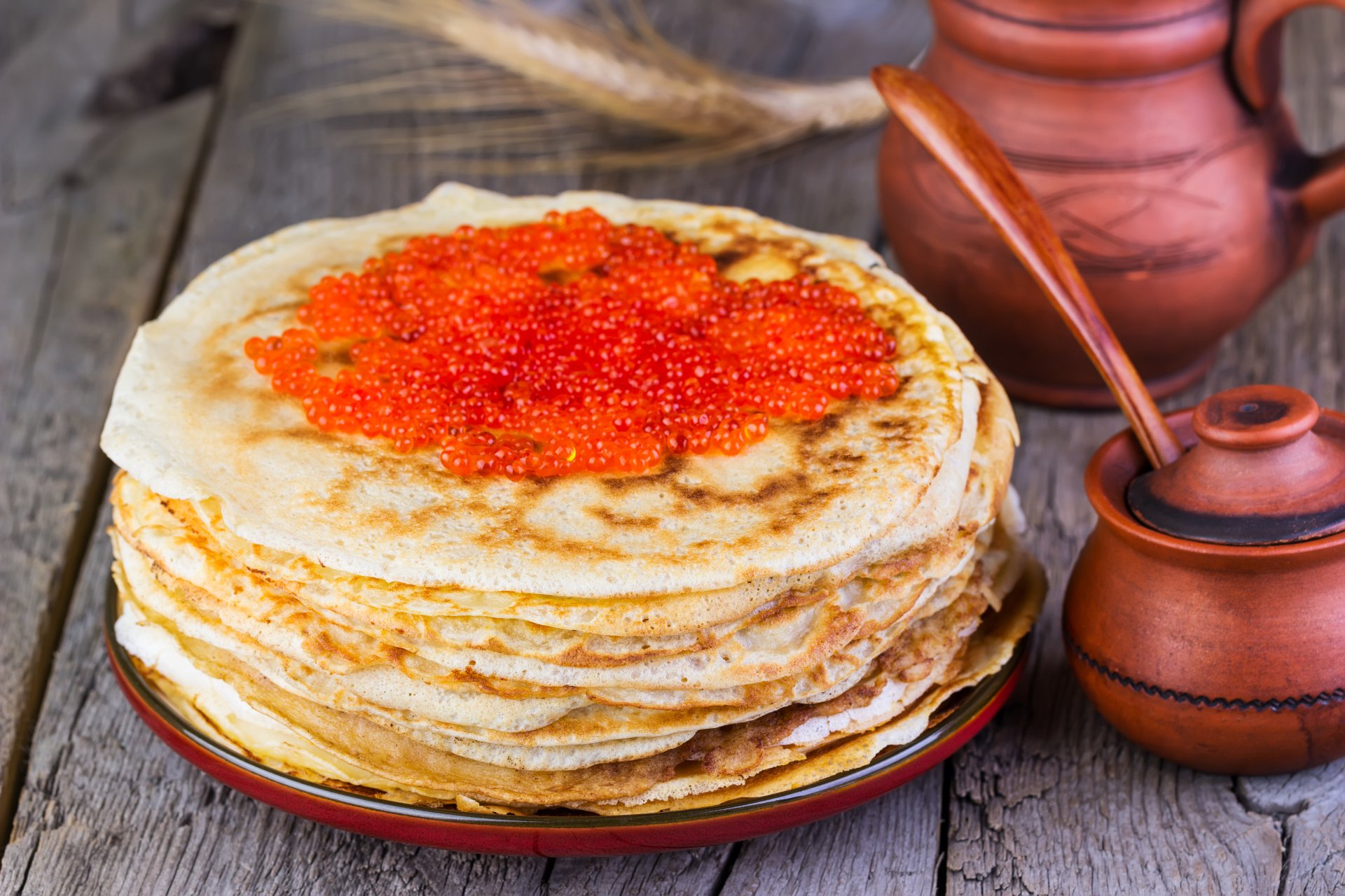 5K Ultra HD PC desktop wallpaper of stacked crêpes topped with bright red caviar on a rustic wooden table, accompanied by ceramic jars and a wooden spoon.