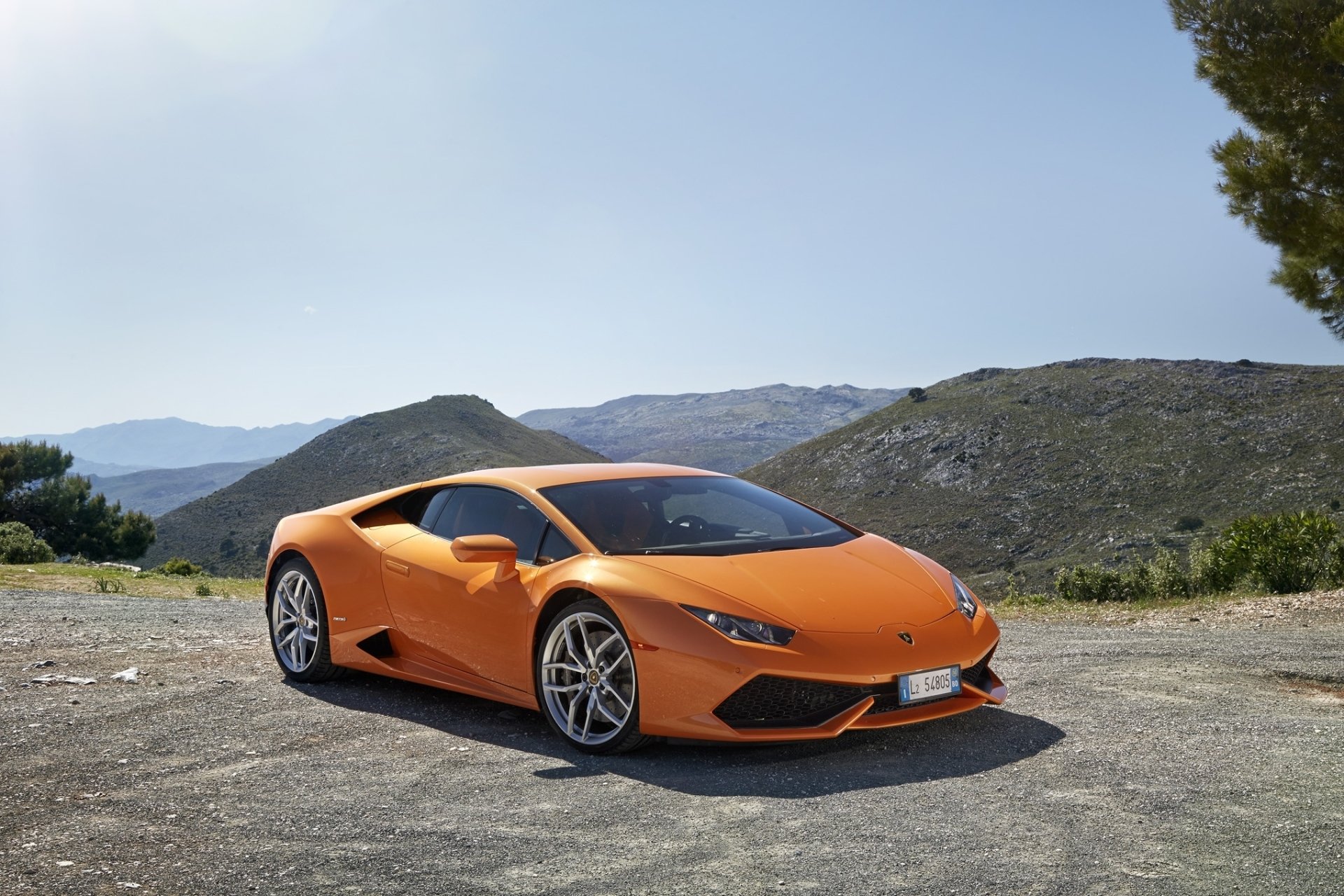 Orange Lamborghini Huracan supercar parked on a scenic mountain road under clear blue skies, displayed as a high-definition PC desktop wallpaper.