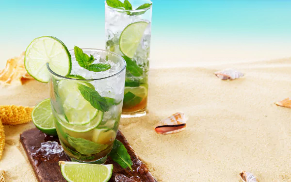 Refreshing mojito cocktails with ice, lime, and mint on sandy beach with seashells, captured in vibrant 4K Ultra HD summer desktop wallpaper and background.