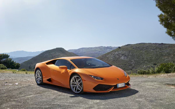 Orange Lamborghini Huracan supercar parked on a scenic mountain road under clear blue skies, displayed as a high-definition PC desktop wallpaper.