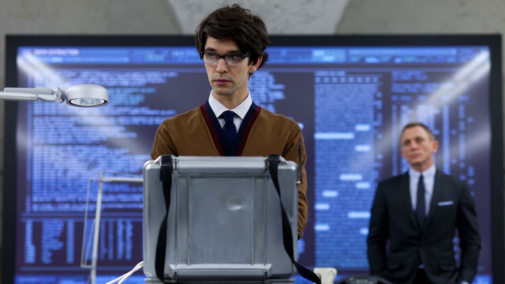 HD desktop wallpaper featuring Ben Whishaw as Q and Daniel Craig as James Bond from the movie Skyfall, with a high-tech background and coding visuals.