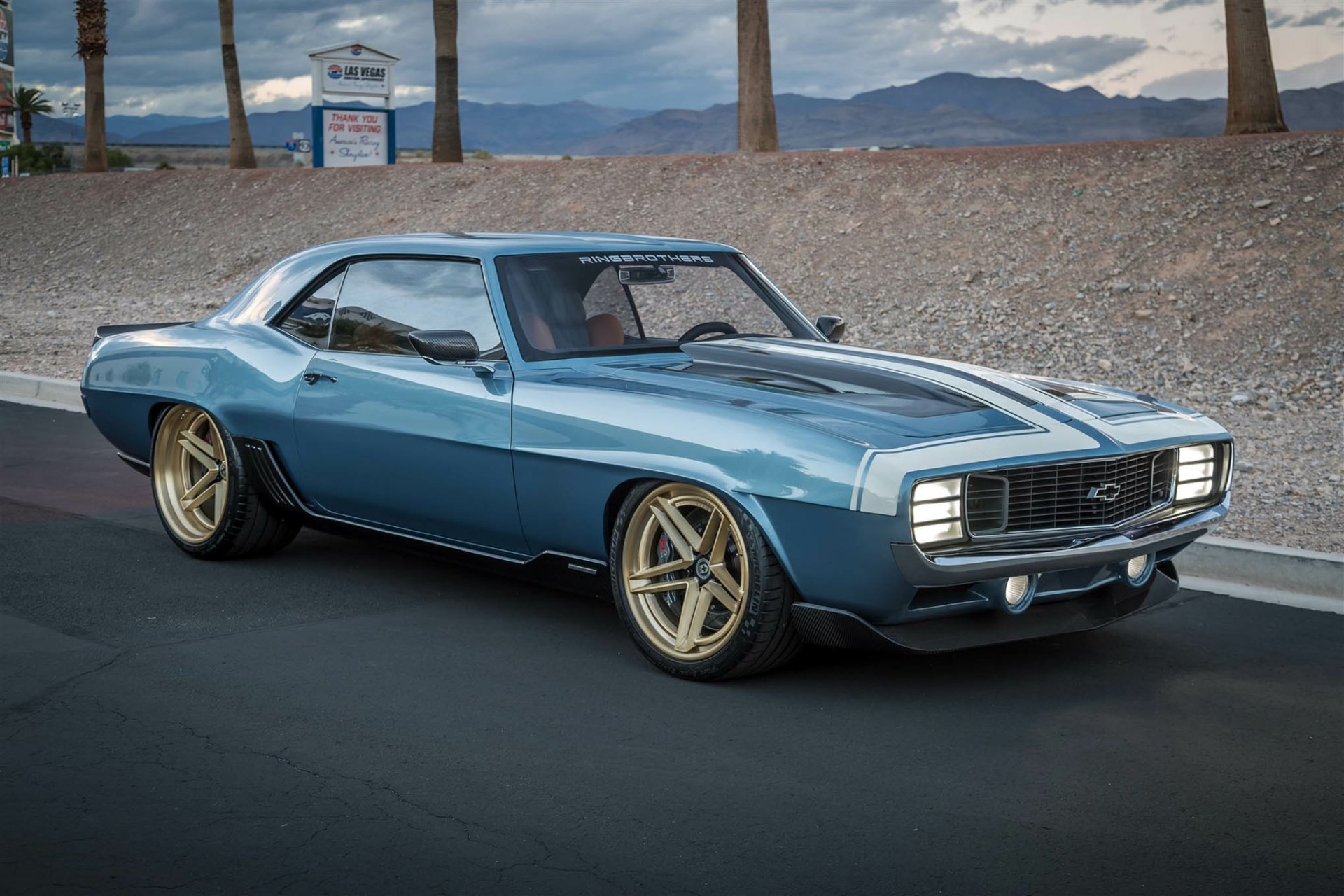 HD desktop wallpaper featuring a sleek Chevrolet Camaro muscle car and hot rod parked on a smooth road with a desert landscape in the background.