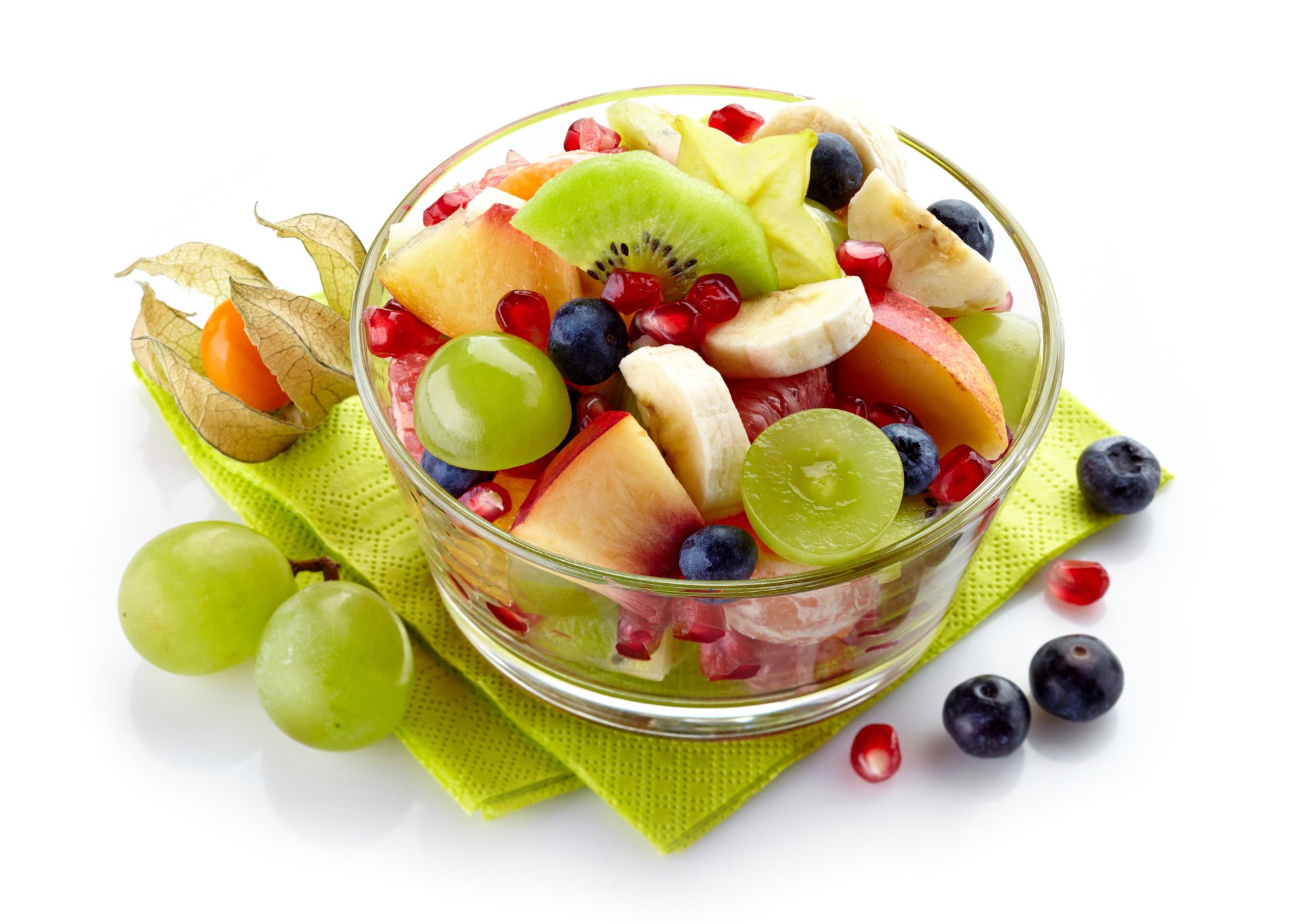 A vibrant fruit salad with banana slices, green grapes, blueberries, kiwi, and pomegranate seeds in a glass bowl on a green napkin, shown in 4K Ultra HD quality.