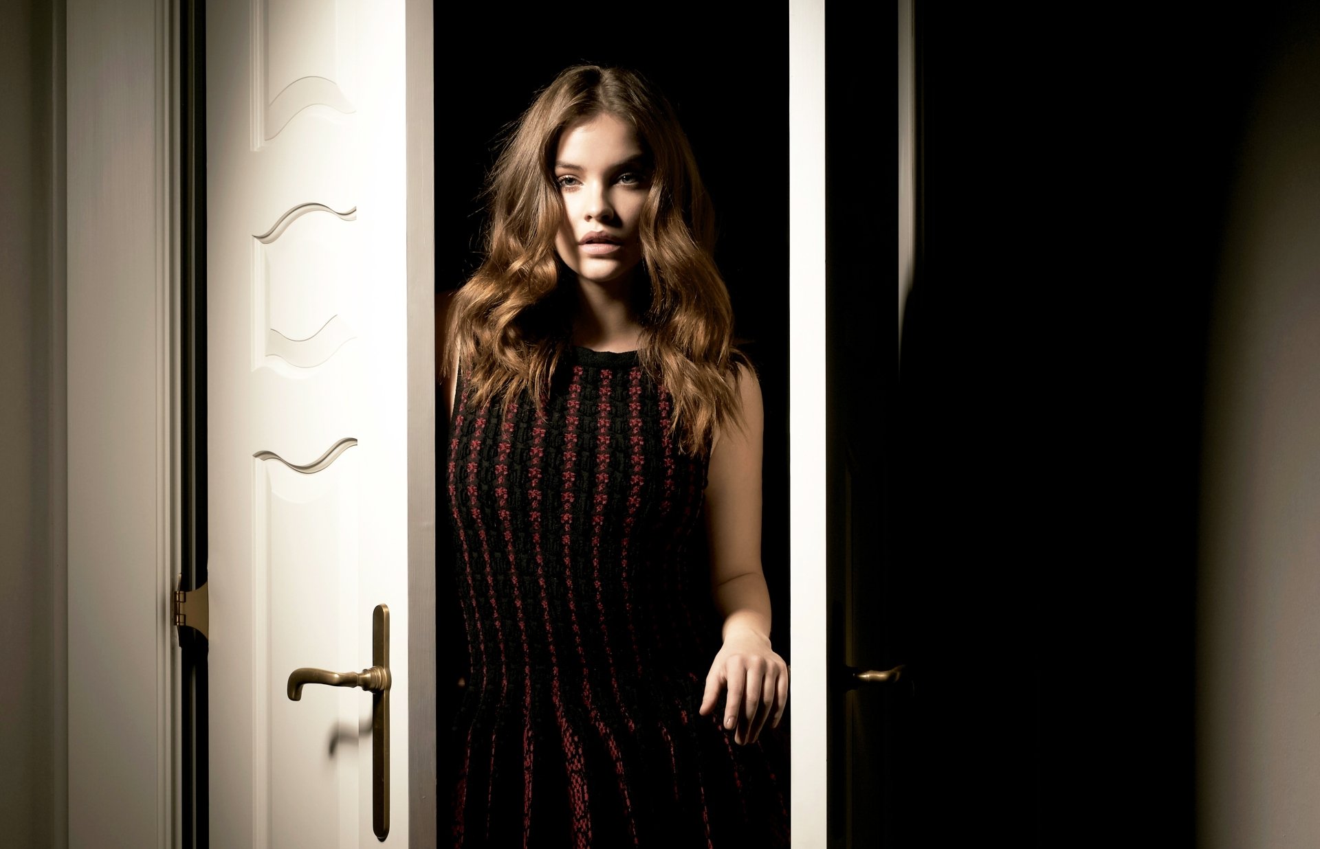 HD desktop wallpaper of Hungarian brunette model and celebrity Barbara Palvin standing in a doorway, illuminated by soft lighting against a dark background.