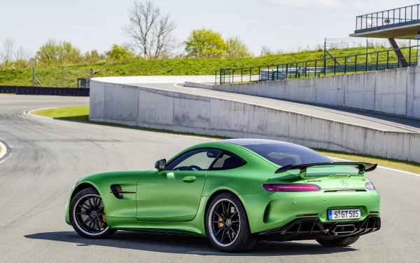HD wallpaper featuring a green Mercedes-AMG GT on a racetrack, showcasing its sleek design and powerful stance against a backdrop of greenery and modern structures.
