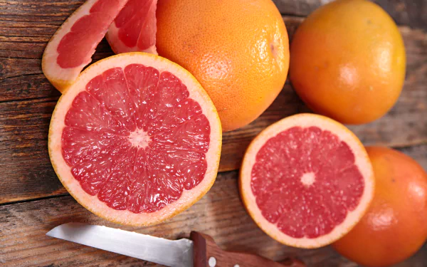 5K Ultra HD PC desktop wallpaper of grapefruit: halved and whole fruit on a rustic wooden surface with a paring knife, vivid pink flesh — fruit/food background