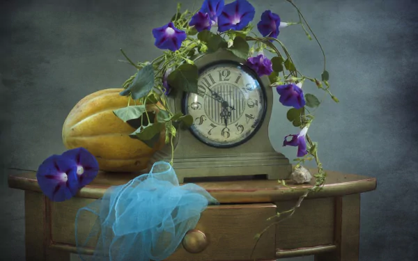 Still life photography featuring a vintage clock draped with a flowering vine, a gourd, and a blue scarf resting on a wooden table, presented as an HD desktop wallpaper.