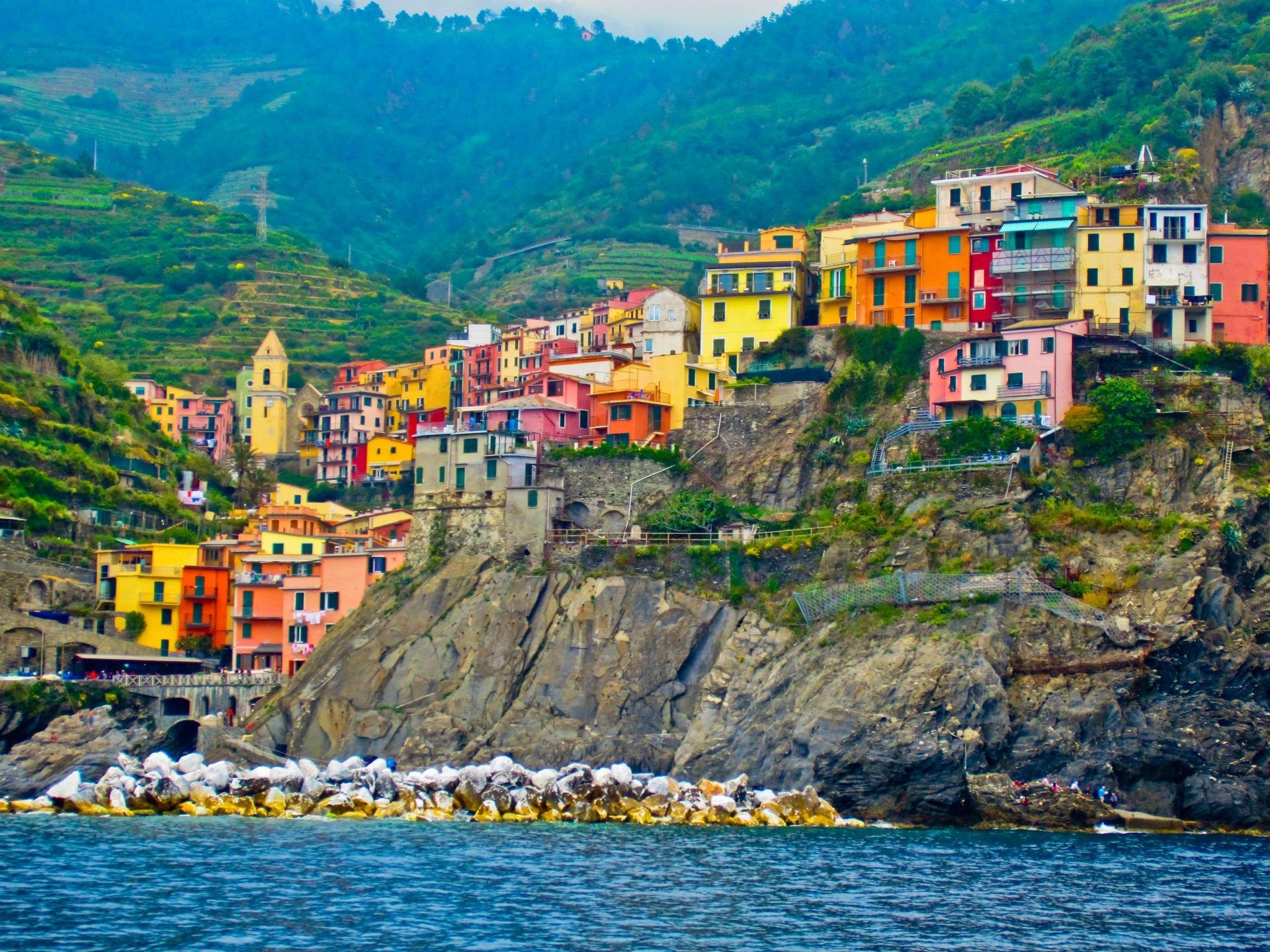 Vibrant village of Manarola in Cinque Terre, Italy, showcasing colorful houses perched on a rocky cliff with a mountain backdrop. HD desktop wallpaper.