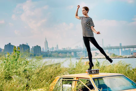 Alicia Vikander, Swedish brunette actress, poses stylishly atop a taxi with a cityscape and river in the background in this HD desktop wallpaper.