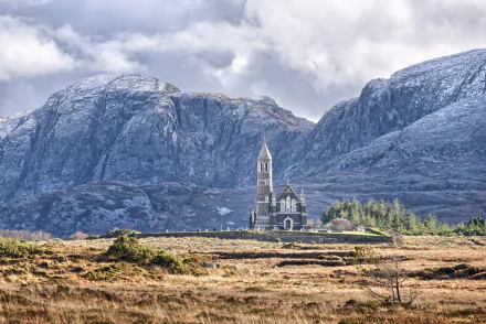 HD desktop wallpaper: Church of the Sacred Heart in rural Ireland, a stone religious church on moorland beneath towering mountains and a dramatic cloudy sky.