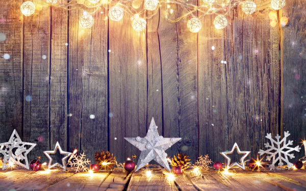 A festive HD desktop wallpaper showing a wooden background adorned with glowing lights, stars, and snowflakes, capturing a warm holiday and Christmas atmosphere.