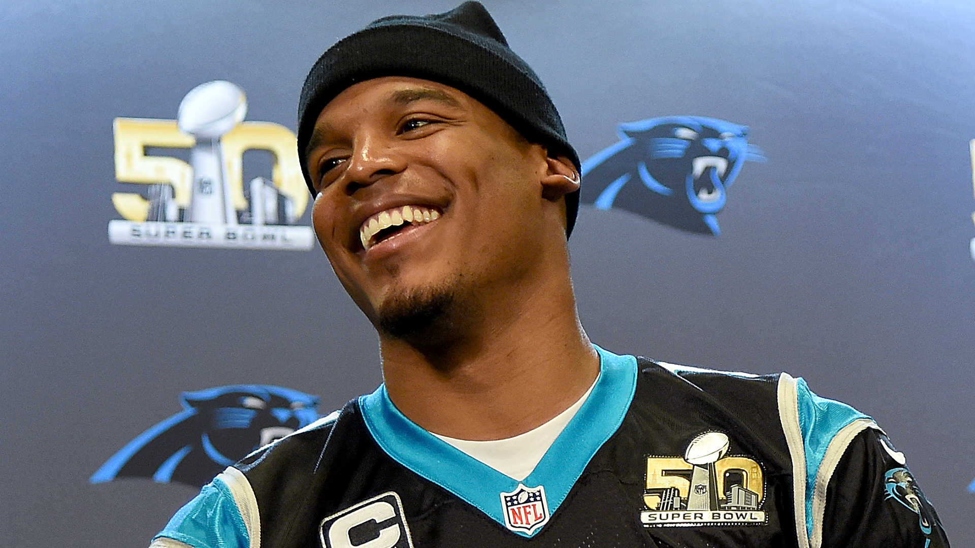 HD wallpaper of Cam Newton smiling at an event, wearing a Carolina Panthers jersey, with a Super Bowl 50 logo in the background.