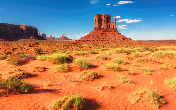HD desktop wallpaper featuring a stunning desert landscape in Monument Valley, Arizona, USA. The horizon reveals red sand and iconic rock formations under a clear blue sky.