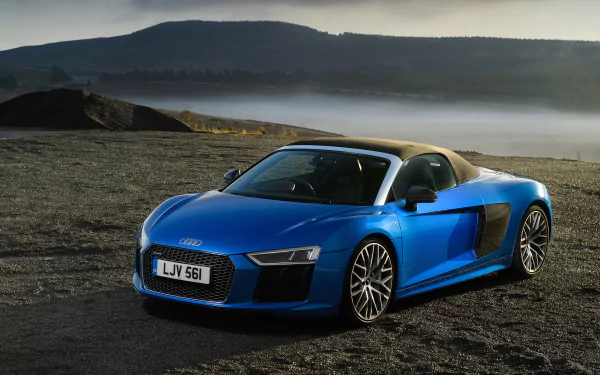 A blue Audi R8 V10 supercar parked on a gravel surface with misty hills and a calm sky in the background, captured in 4K Ultra HD quality.