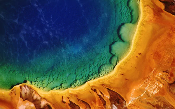 A stunning aerial view of a vibrant geothermal pool in Yellowstone National Park, capturing nature's vivid blue, green, and orange hues. This high-definition image serves as a breathtaking desktop wallpaper.