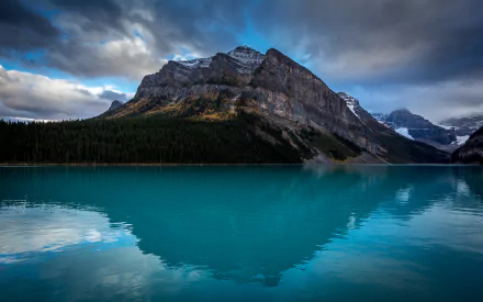 Turquoise Lake Louise in Alberta, Canada, showcases a serene mountain landscape with dense forest and dramatic clouds, captured in stunning HD.