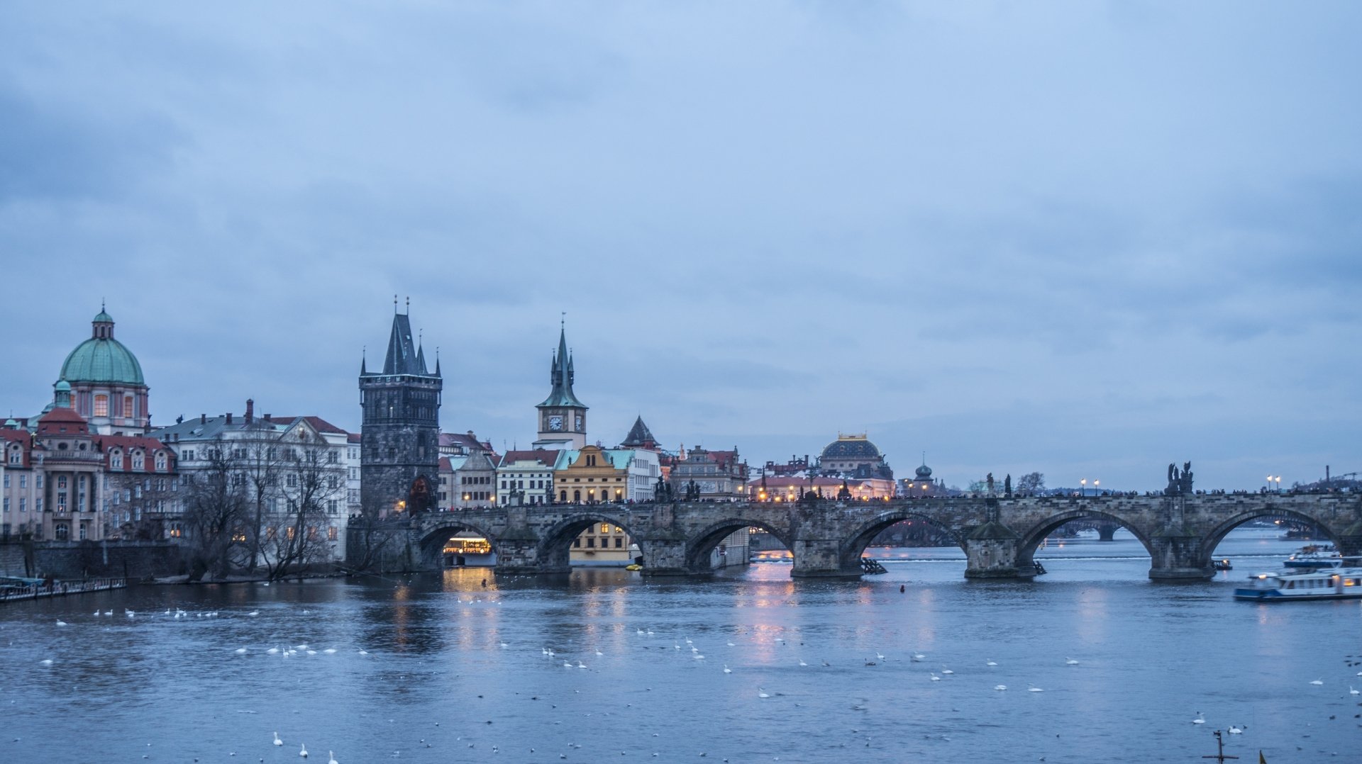 5K Ultra HD desktop wallpaper of Charles Bridge in Prague, Czech Republic, spanning the Vltava River at dusk with the historic skyline and bridge arches reflected in calm water.