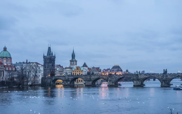 5K Ultra HD desktop wallpaper of Charles Bridge in Prague, Czech Republic, spanning the Vltava River at dusk with the historic skyline and bridge arches reflected in calm water.