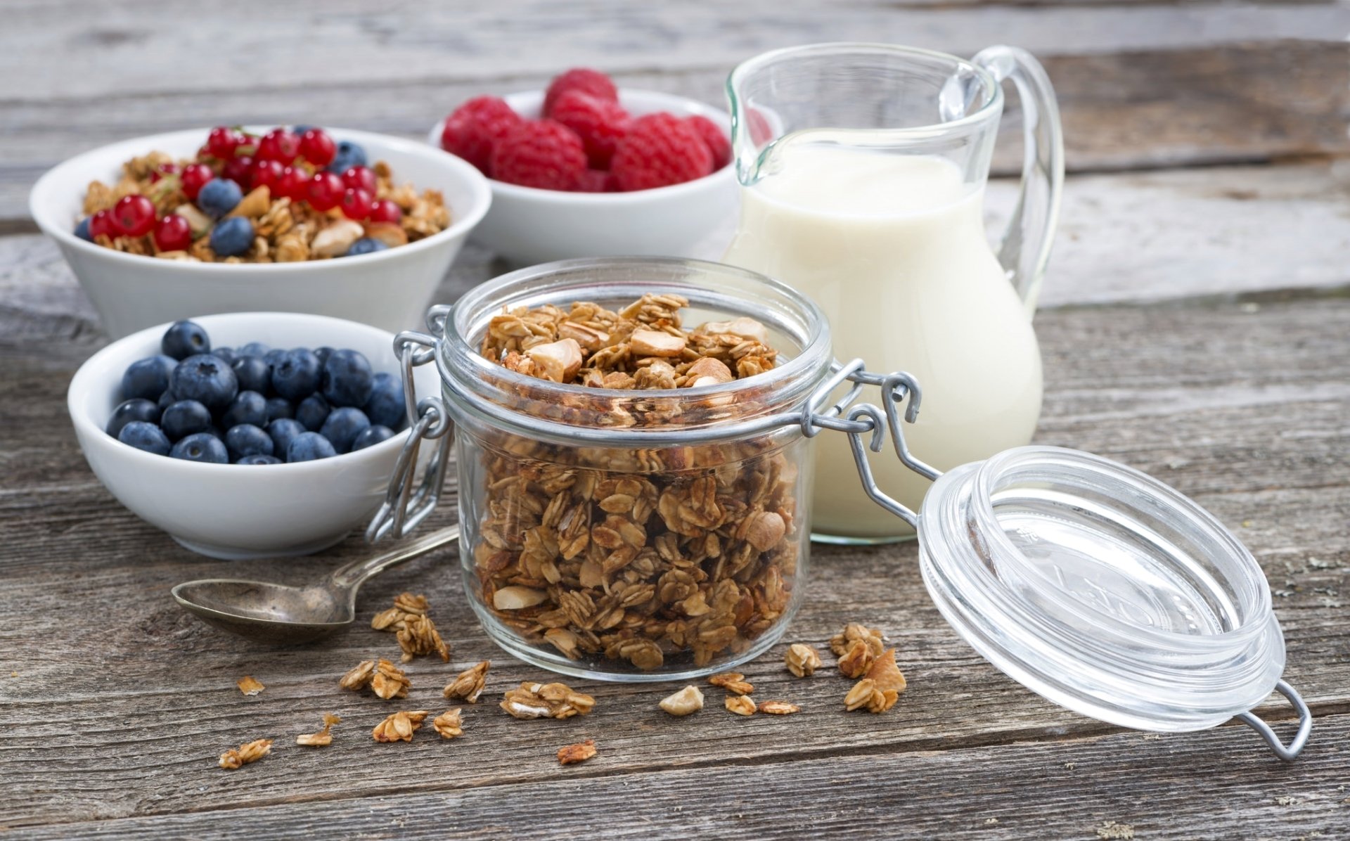 A still life HD desktop wallpaper featuring fresh blueberries, raspberries, muesli, and a glass jug of milk on a rustic wooden surface for a vibrant breakfast scene.